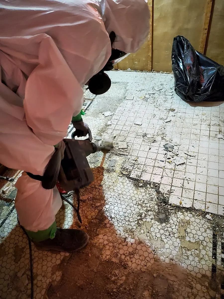 Technician in protective suit removing old asbestos floor tile and mastic during a Winnipeg abatement project