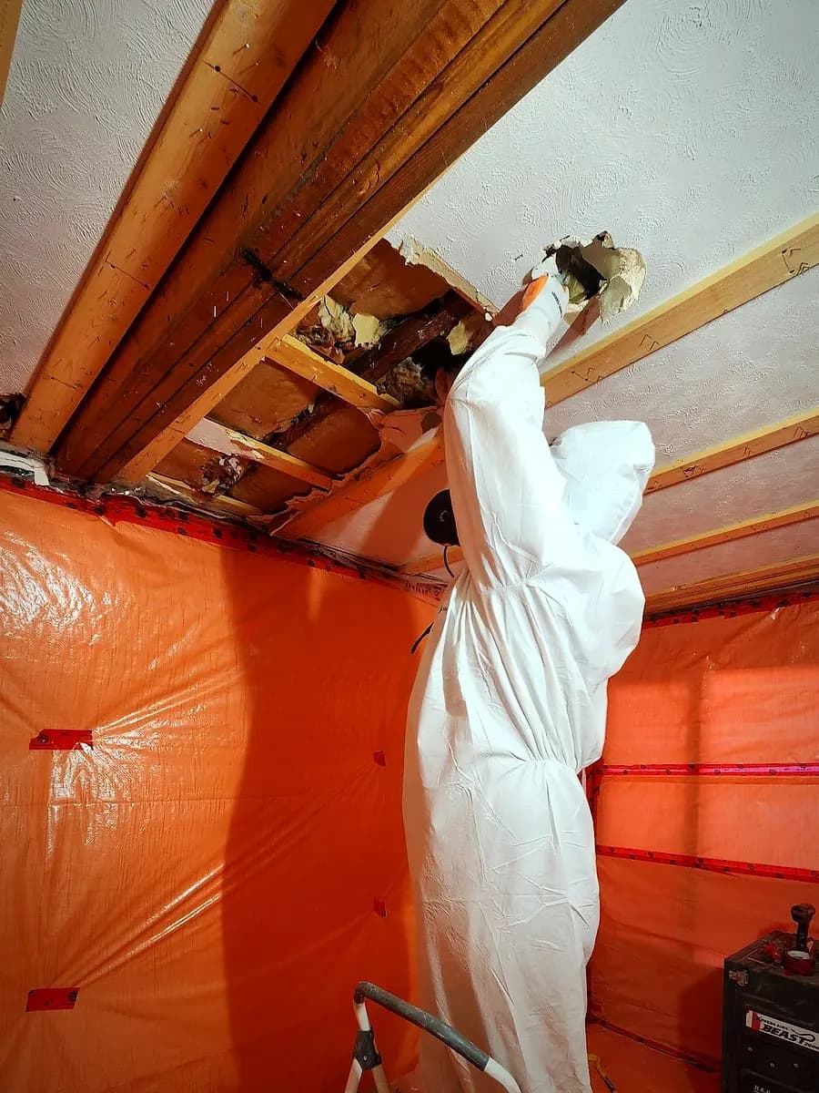 Relief Restorations technician removing a textured asbestos ceiling inside sealed orange containment in a Winnipeg home