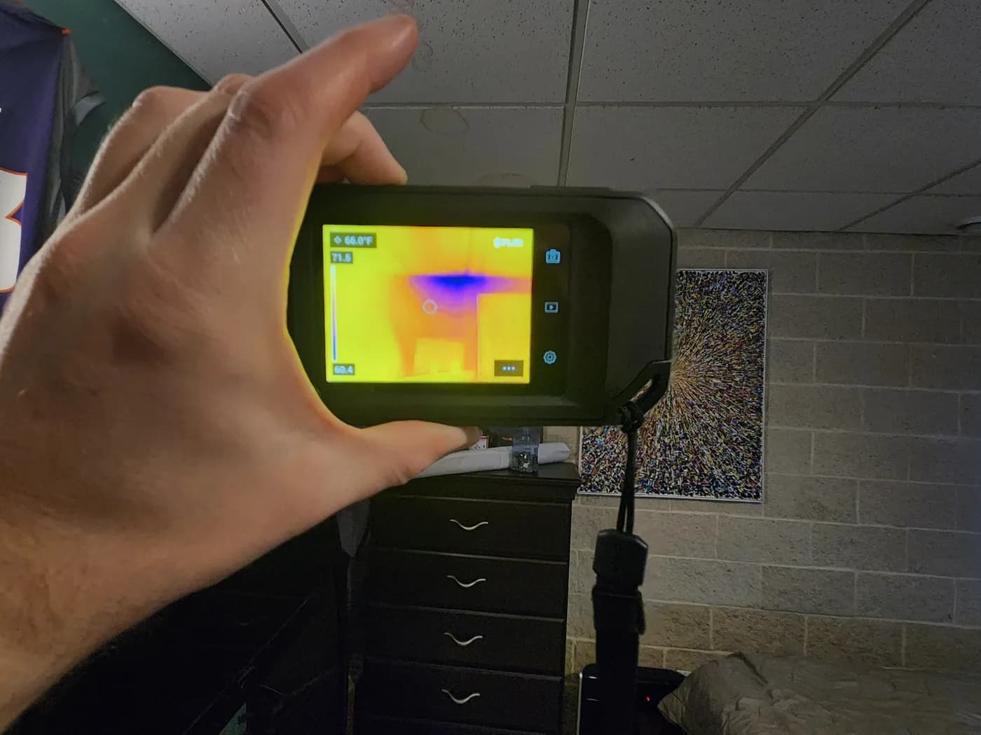 Relief Restorations technician scanning a wall with a FLIR thermal imaging camera, the display showing a cool blue area that flags hidden moisture behind the surface.
