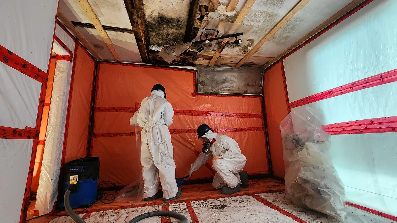 Two Relief Restorations technicians in protective suits removing mould inside a sealed containment in a Winnipeg home