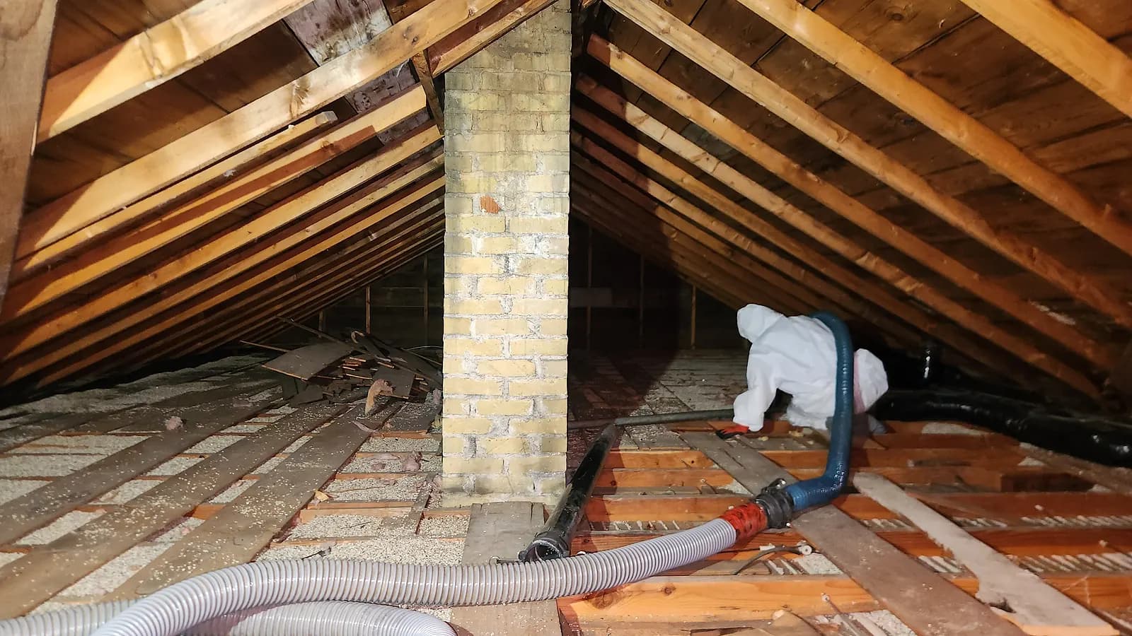 Relief Restorations technician in a protective suit vacuuming vermiculite insulation from a Winnipeg attic with a HEPA removal system